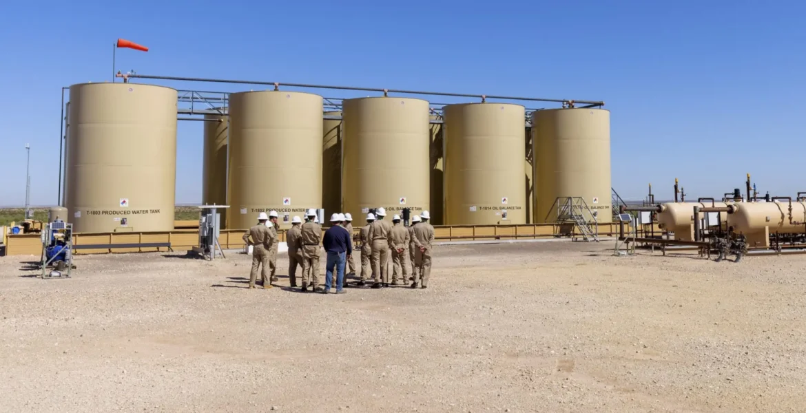 Five light brown cylinder tanks with workers standing in front of them